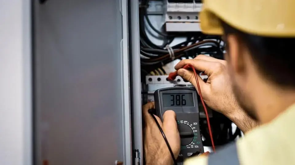 Electrician using a digital multimeter to test voltage inside an electrical panel, ensuring safe and accurate diagnostics.