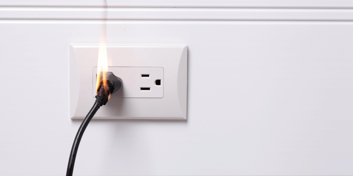 Burning electrical plug connected to a wall outlet, showing a common electrical fire hazard in the home.
