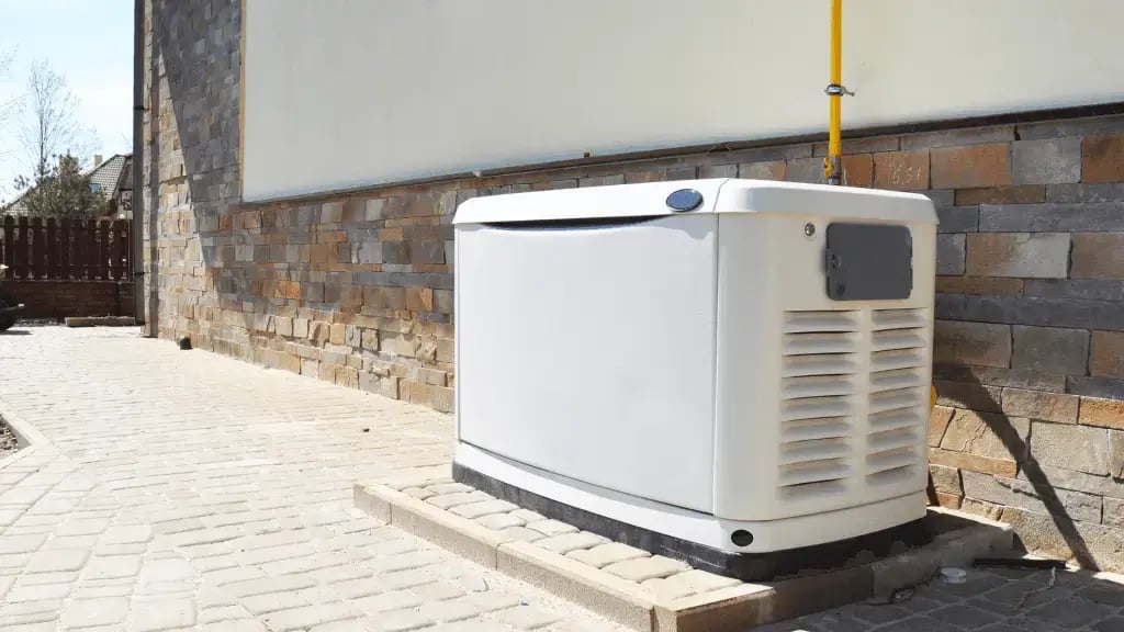 A standby home generator installed on a concrete pad beside a brick and stone exterior wall, connected to a yellow fuel line for backup power.