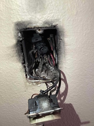 Outlet pulled away from a wall showing a WAGO wire connector but the outlet has caught fire causing black marks on wall.