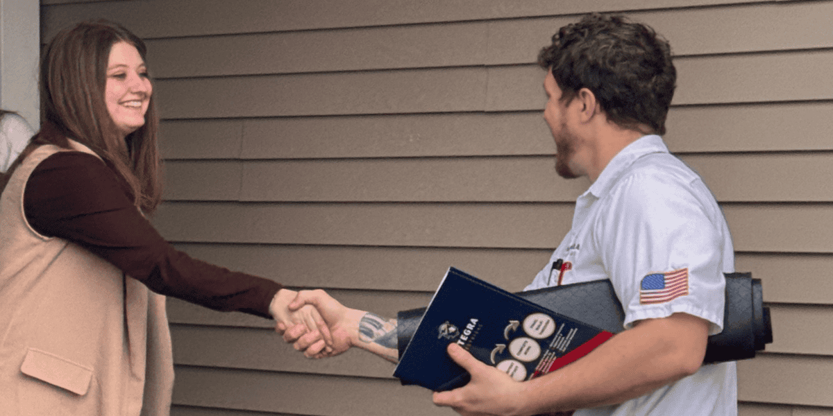 Integra electrician shaking hands with a smiling homeowner outside her home, holding project documents and wearing a white uniform with an American flag patch.