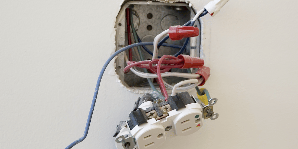 Unsafe loose outlet with tangled wires inside a wall box, showing why professional electrical repair matters.