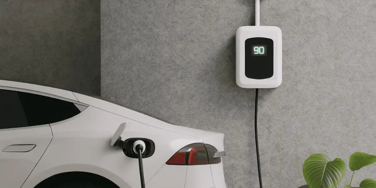 White electric car charging in a modern garage with a wall-mounted EV charger showing 90% charge on digital display.