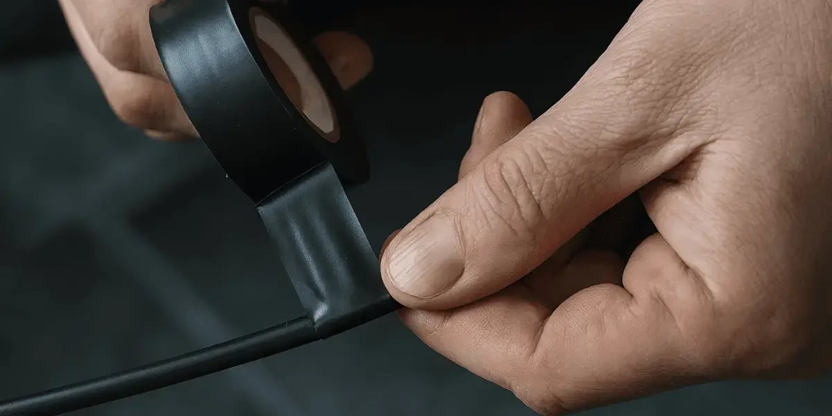 Close-up of hands wrapping black electrical tape tightly around a wire, with the focus on the tape being stretched and pressed into place.