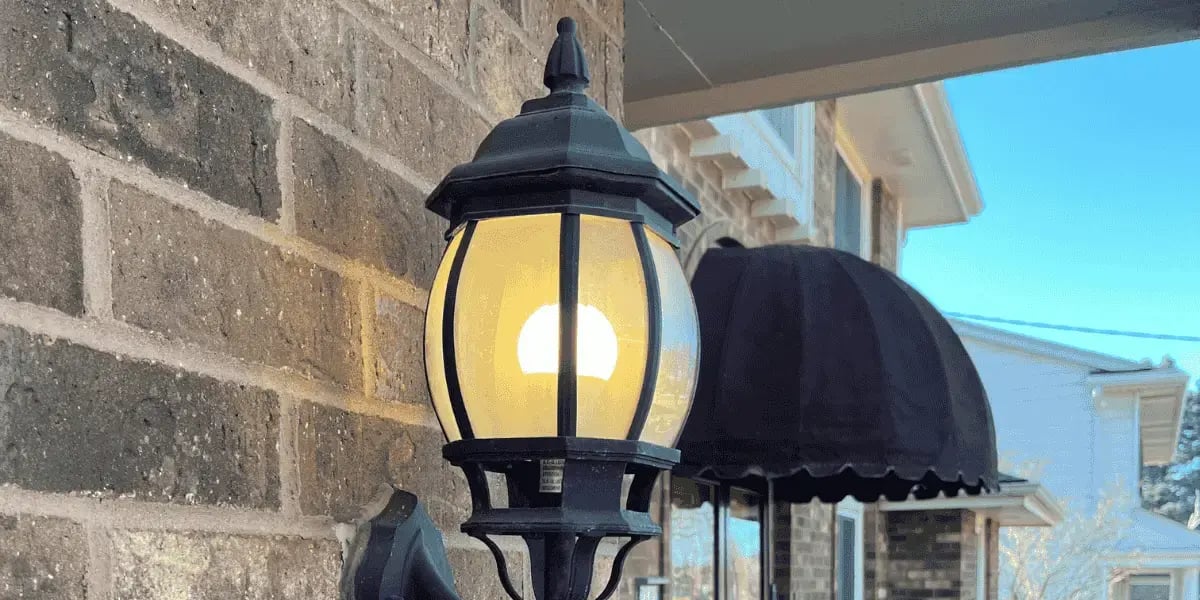 A lantern style light fixture hanging on a brick wall outside 
