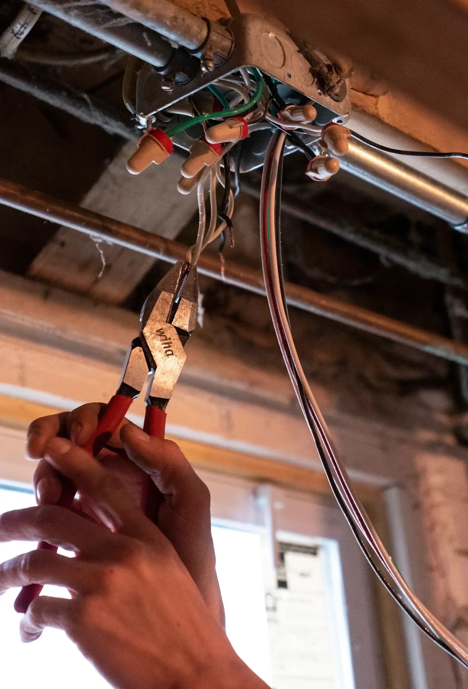 Electrician using pliers to cut or strip electrical wiring during a home wiring upgrade in a basement or unfinished space.