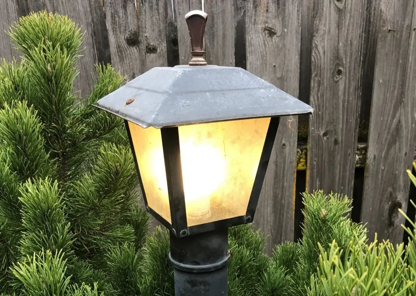 An outdoor lamp by a fence with landscaping
