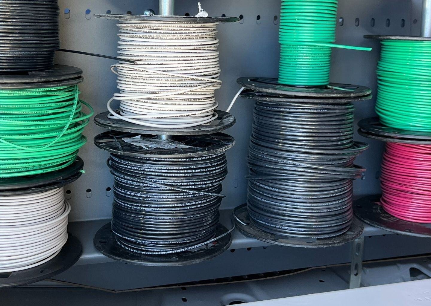 Spools of electrical wire in various colors, including black, white, green, and red, organized on a shelf inside a service vehicle.