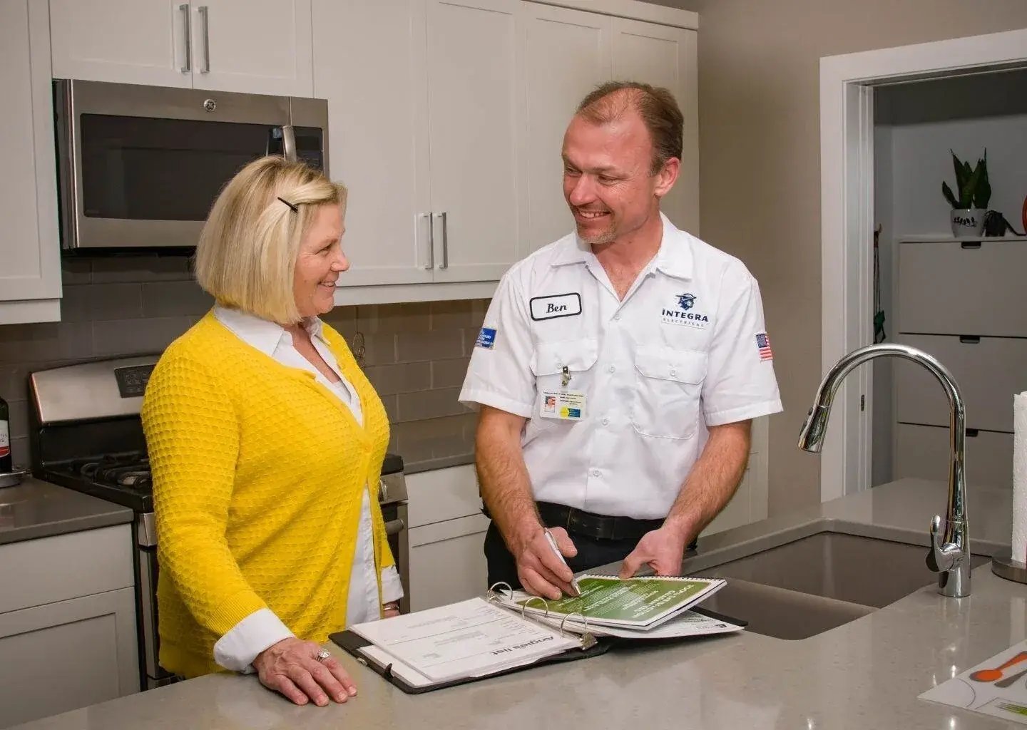 Integra Electrical technician talking with a homeowner in a kitchen while reviewing an inspection checklist and explaining electrical service options.