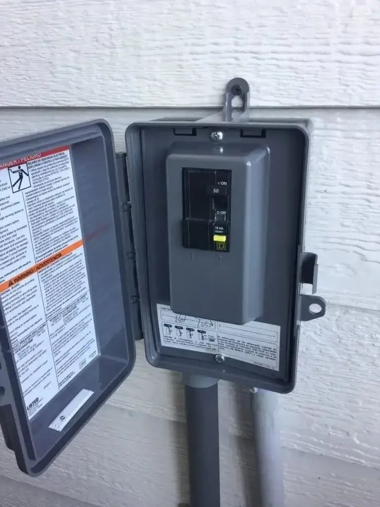 Close-up of an outdoor electrical disconnect switch with labeled circuit breakers and safety warning stickers.