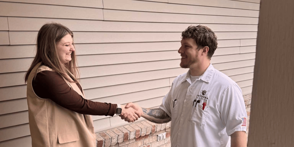 Homeowner shaking hands with an Integra Electrical technician outside a house.