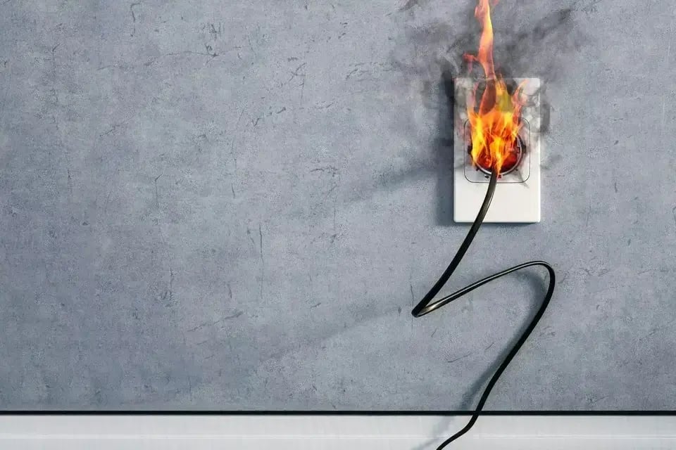 Electrical outlet on a gray wall with a burning cord and visible flames.
