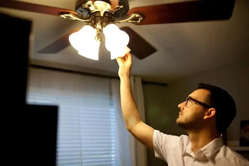 Electrician changing the bulb in a ceiling fan light fixture