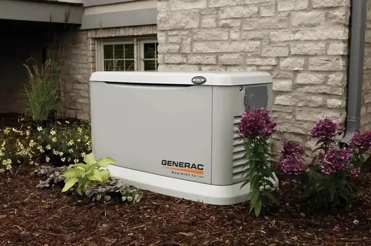 Generac Guardian Series standby generator installed outside a home surrounded by landscaping, providing backup power during outages.