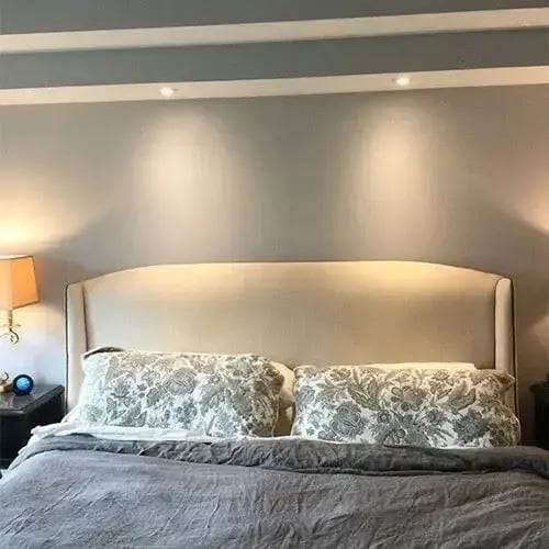 Bedroom with gray accent wall, upholstered headboard, and soft ambient lighting above the bed
