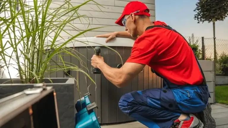 Technician using a power drill while working on the exterior panel of a hot tub.