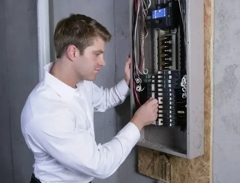 Electrician inspecting and adjusting wiring inside a residential electrical breaker panel to ensure safe operation.