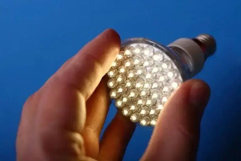 Person holding an illuminated LED light bulb against a blue background.