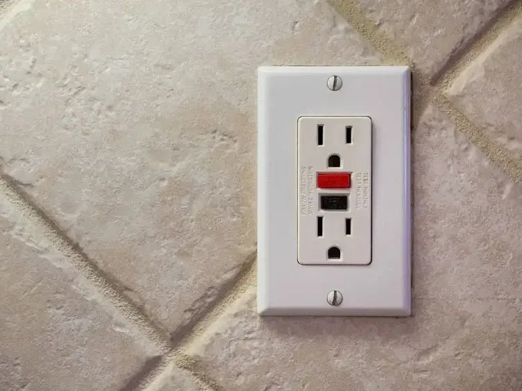 GFCI electrical outlet with test and reset buttons installed on a tiled wall.