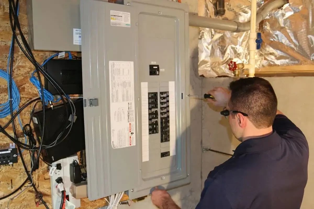 Electrician installing or inspecting a residential breaker panel in a basement, ensuring proper wiring and safety compliance