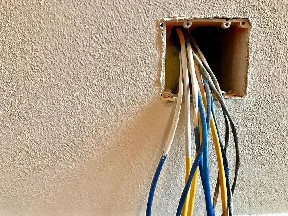 Exposed electrical wires extending from a wall outlet box during residential rewiring or electrical repair work.