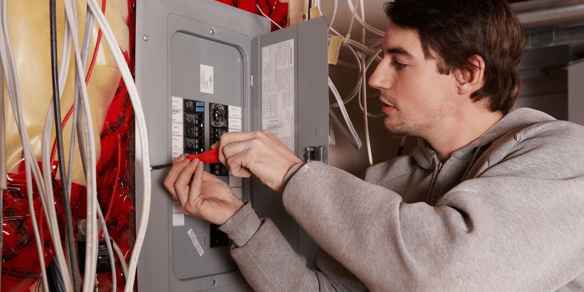 Electrician working inside a residential electrical panel with exposed wiring.