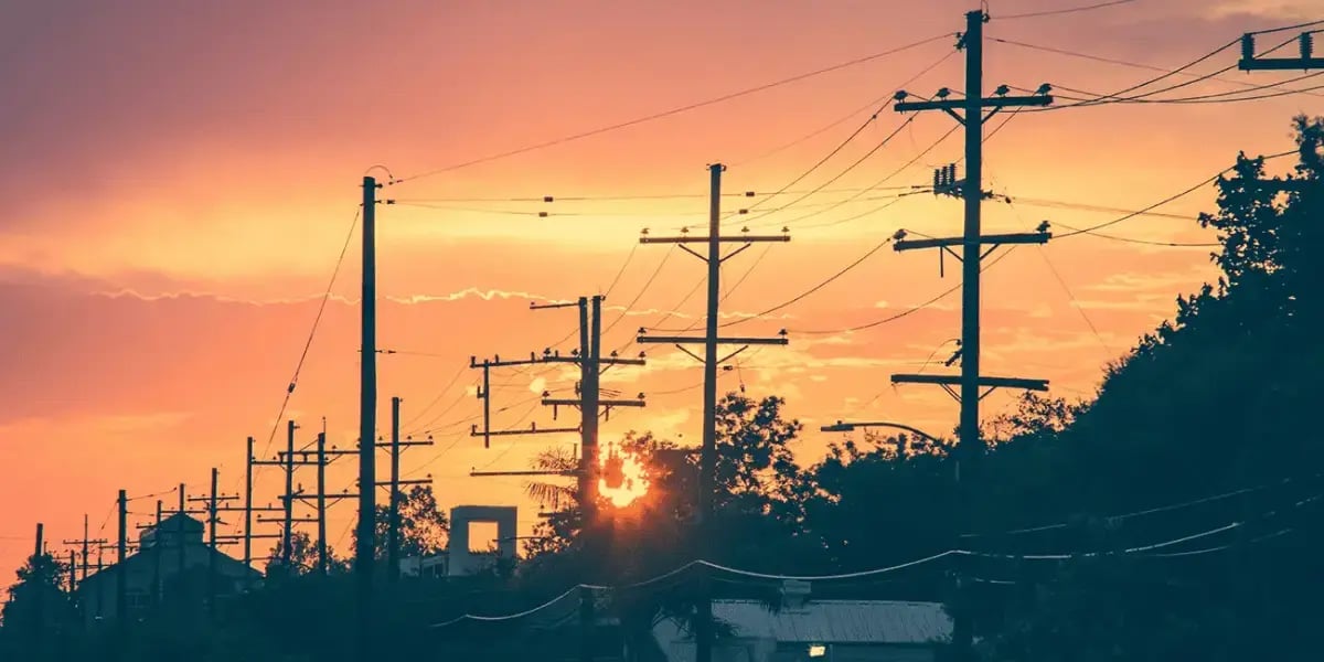 A row of utility poles and power lines silhouetted by the sunset